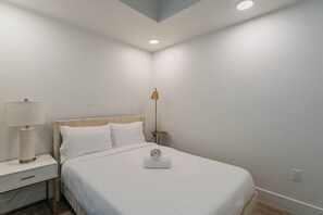 A neatly made bed with white linens, a bedside lamp, and a small table with a lamp. - Saiya  1118 (Phoenix)