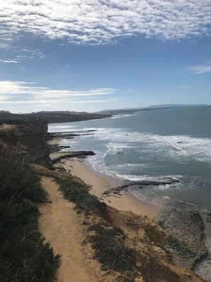 Eine Küstenlandschaft mit einem sandigen Pfad, der zum Meer führt, felsigen Klippen und einem klaren Himmel.