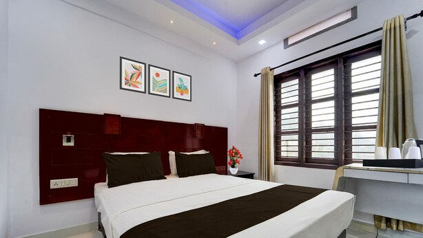 A hotel room with a large bed, a desk with a chair, a window with curtains, and artwork on the wall.