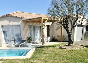 Ein Haus mit Pool, einer überdachten Terrasse und Gartenmöbeln sowie ein Baum im Garten.