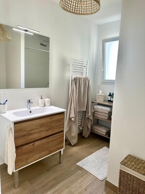 Ein modernes Badezimmer mit einem weißen Waschtisch, Hol Schubladen, einem großen Spiegel, einem Handtuchhalter und einem Fenster.