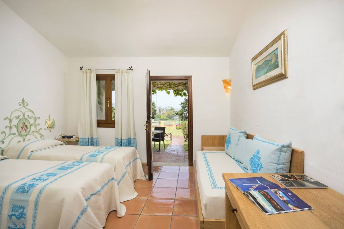 A room with two beds, a wooden bench, a table with a magazine, and a door leading to an outdoor area.