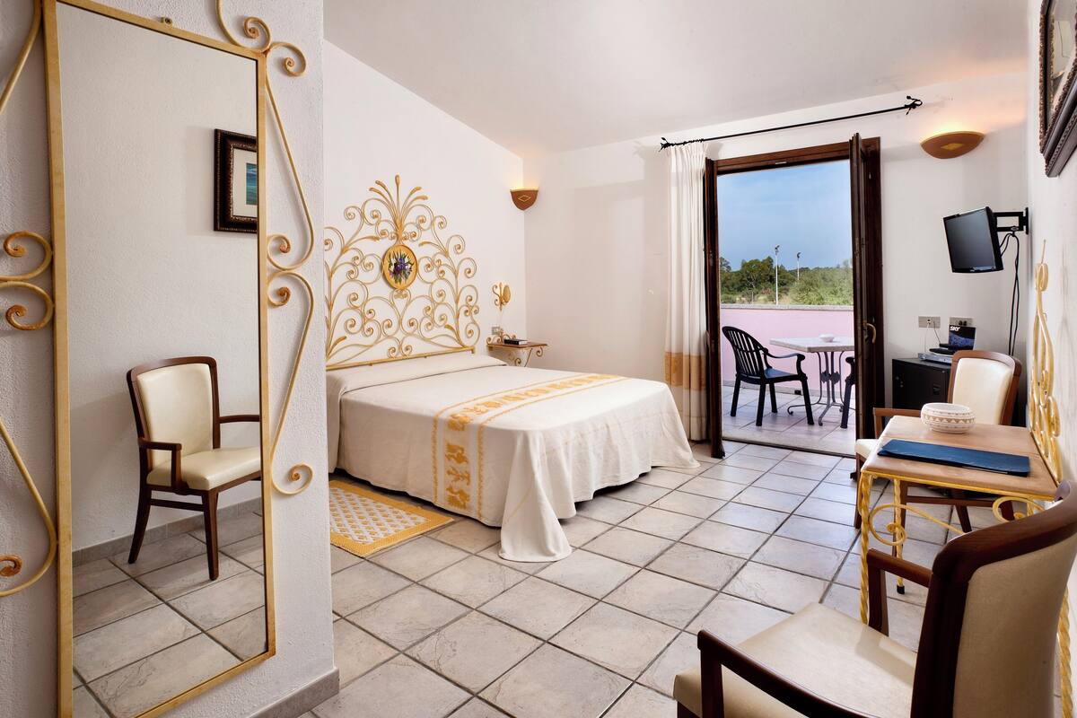 A hotel room with a bed, a chair, a desk with a laptop, and a view of the outdoors.