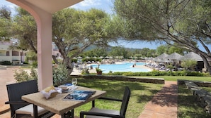 A patio with a table and chairs, overlooking a swimming pool and lounge area with umbrellas. - Hotel with swimming pool near Baja Sardinia (Arzachena)