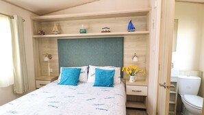 A bedroom with a bed, nightstands, a dresser, a mirror, and a bathroom with a toilet and sink. - Beachcombers (Wareham)