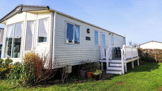 A mobile home with a porch, a small garden, and a clear sky. - Beachcombers (Wareham)
