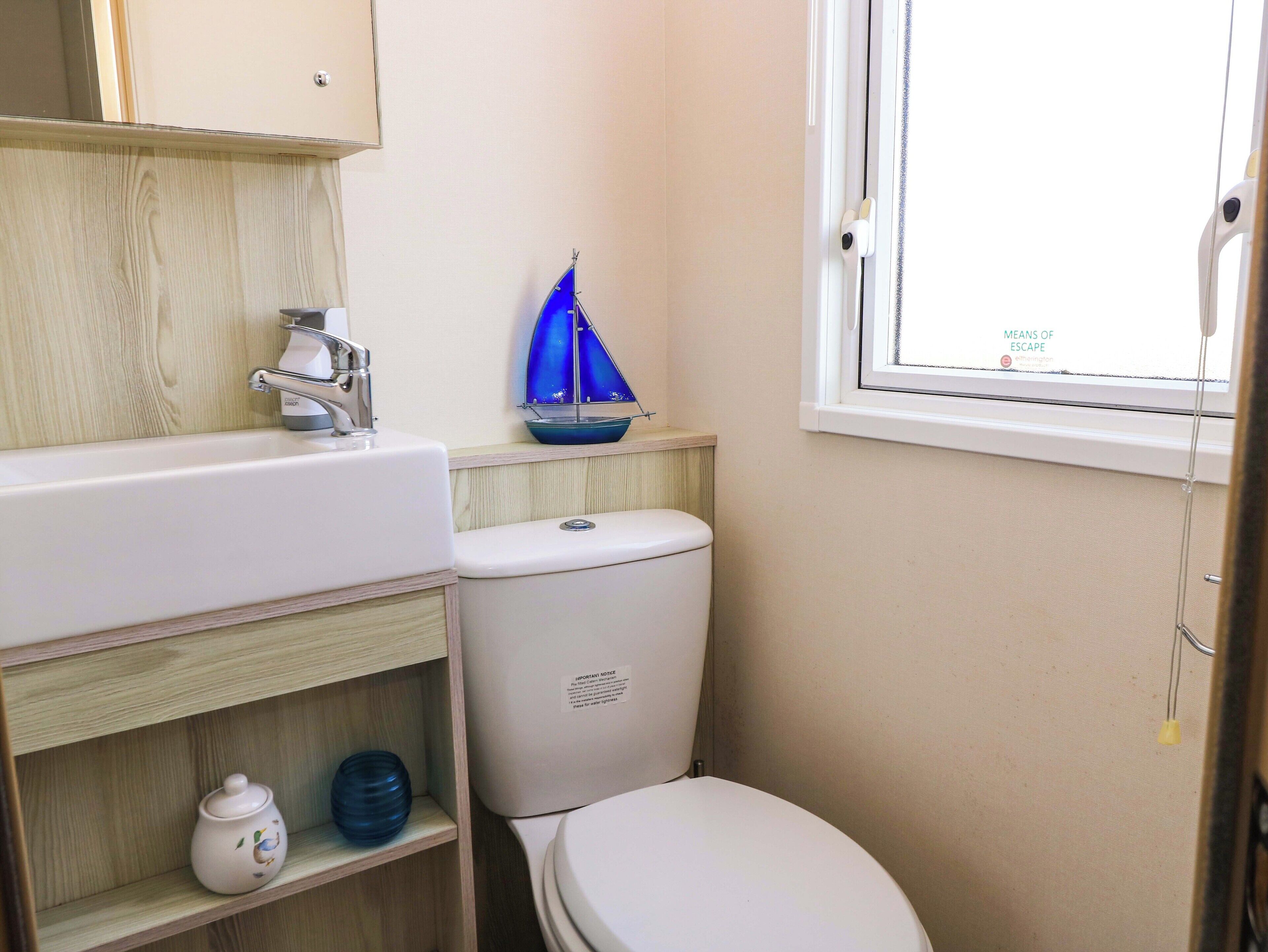 Un bagno con un lavandino bianco, un WC, una piccola mensola con un oggetto decorativo e una finestra vista cielo.