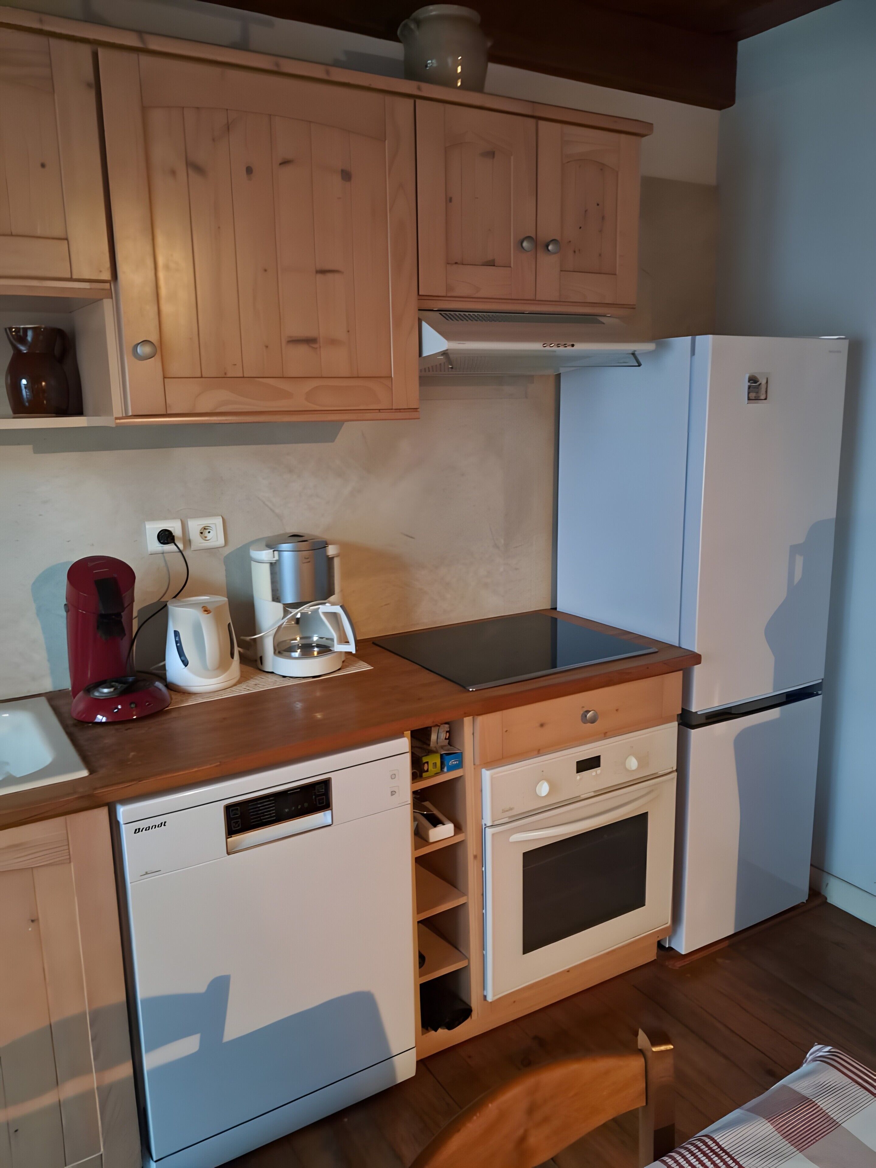 A compact kitchen with wooden cabinets, a white dishwasher, a built-in oven, and a refrigerator.