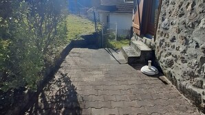 A paved pathway leading to a stone building with a metal fence and a chimney. - Gîte du lavoir: Village House in the Countryside (Champs sur Tarentaine Marchal)