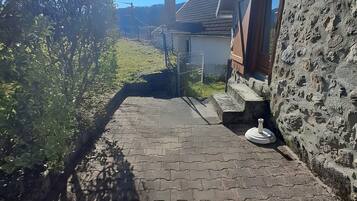Un chemin pavé mène à un bâtiment en pierre, entouré d’une clôture en métal et doté d’une cheminée.