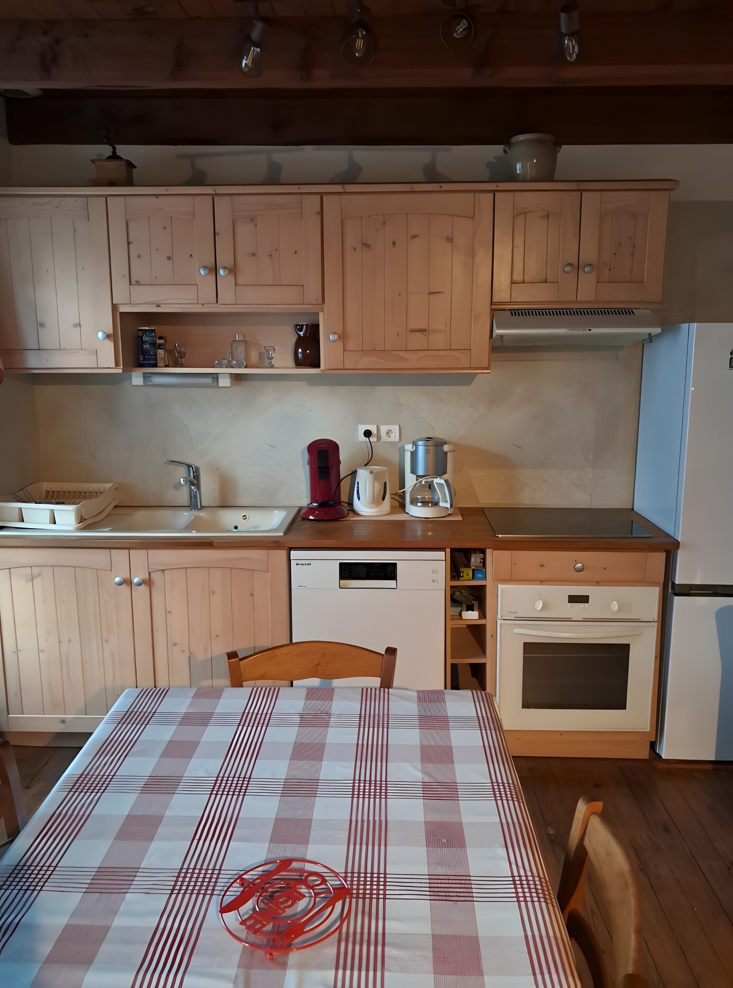 A kitchen with wooden cabinets, a dishwasher, a coffee maker, and a table with a checkered tablecloth.