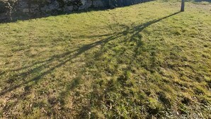 A grassy field with a stone wall and a hill in the background. - Gîte du lavoir: Village House in the Countryside (Champs sur Tarentaine Marchal)