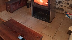 A stone wall with a wood-burning stove, a wooden bench, and a tiled floor. - Gîte du lavoir: Village House in the Countryside (Champs sur Tarentaine Marchal)