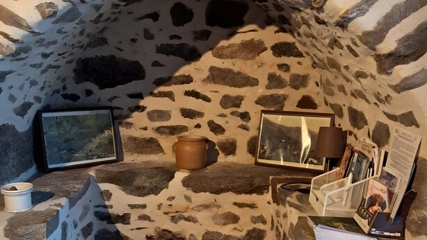 A stone-walled room with a fireplace, a television, and a small table with a candle. - Gîte du lavoir: Village House in the Countryside (Champs sur Tarentaine Marchal)