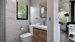 Une salle de bain moderne équipée de toilettes, d’un lavabo et d’une douche. Une fenêtre offre une vue sur les arbres.
