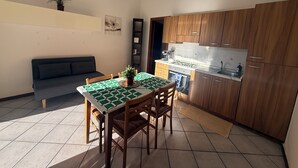 Uma cozinha compacta com armários de madeira, uma mesa de jantar com toalha xadrez e um sofá em uma pequena sala de estar.