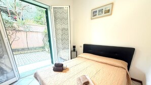 Quarto com uma cama, mesa de cabeceira, quadro emoldurado e vista através de uma porta de vidro.