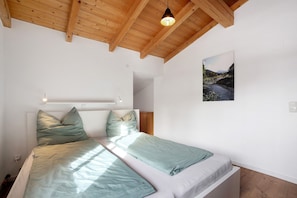 Een slaapkamer met een houten plafond, een bed met groene beddengoed, een nachtkastje en een aan de muur hangend schilderij.