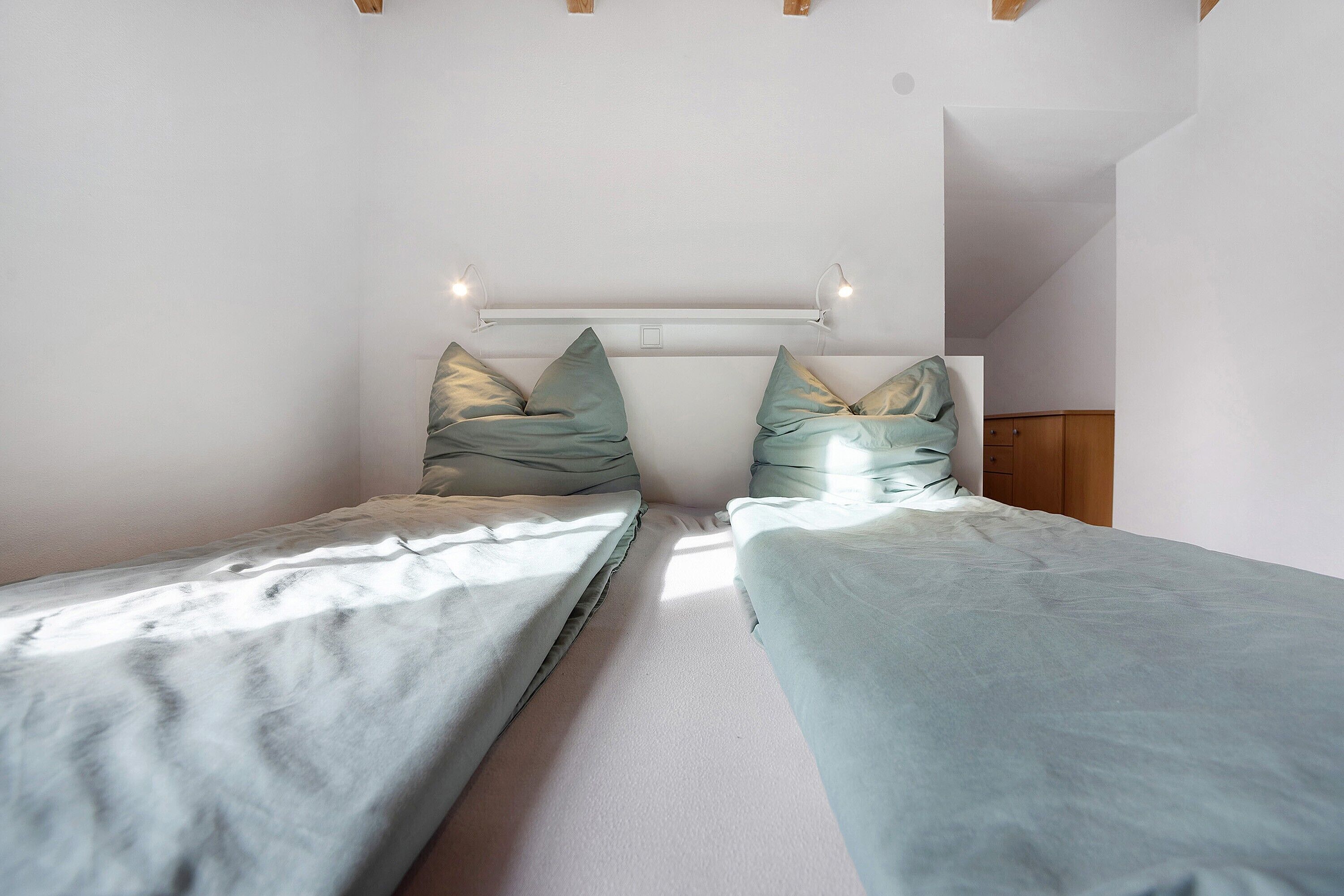 Une chambre avec deux lits simples, une tête de lit dotée de lampes et une armoire en bois.