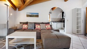 A living room with a sectional sofa, a white coffee table, a floor lamp, and an arched doorway leading to a kitchen. - Apartment 'Schnitzer' with Balcony and Wi-Fi (Görisried)