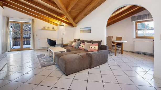 A spacious living area with a wooden ceiling, a sofa set, a dining table, and a view through a glass door. - Apartment 'Schnitzer' with Balcony and Wi-Fi (Görisried)