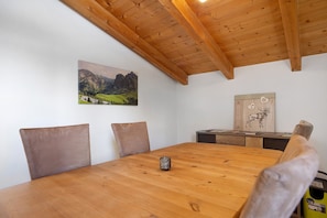Een houten eettafel met stoelen, een kaars, een schilderij van bergen, en een houten kastje met een illustratie van een hert.