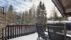 A wooden deck with snow, metal chairs, and a view of trees and buildings. - Apartment 'Schnitzer' with Balcony and Wi-Fi (Görisried)