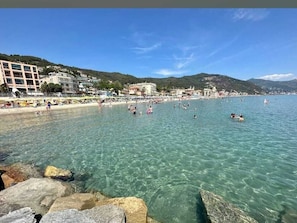 A coastal beach with clear water, rocky shoreline, and buildings in the background. - Terrazza vista Laigueglia fronte mare (Laigueglia)