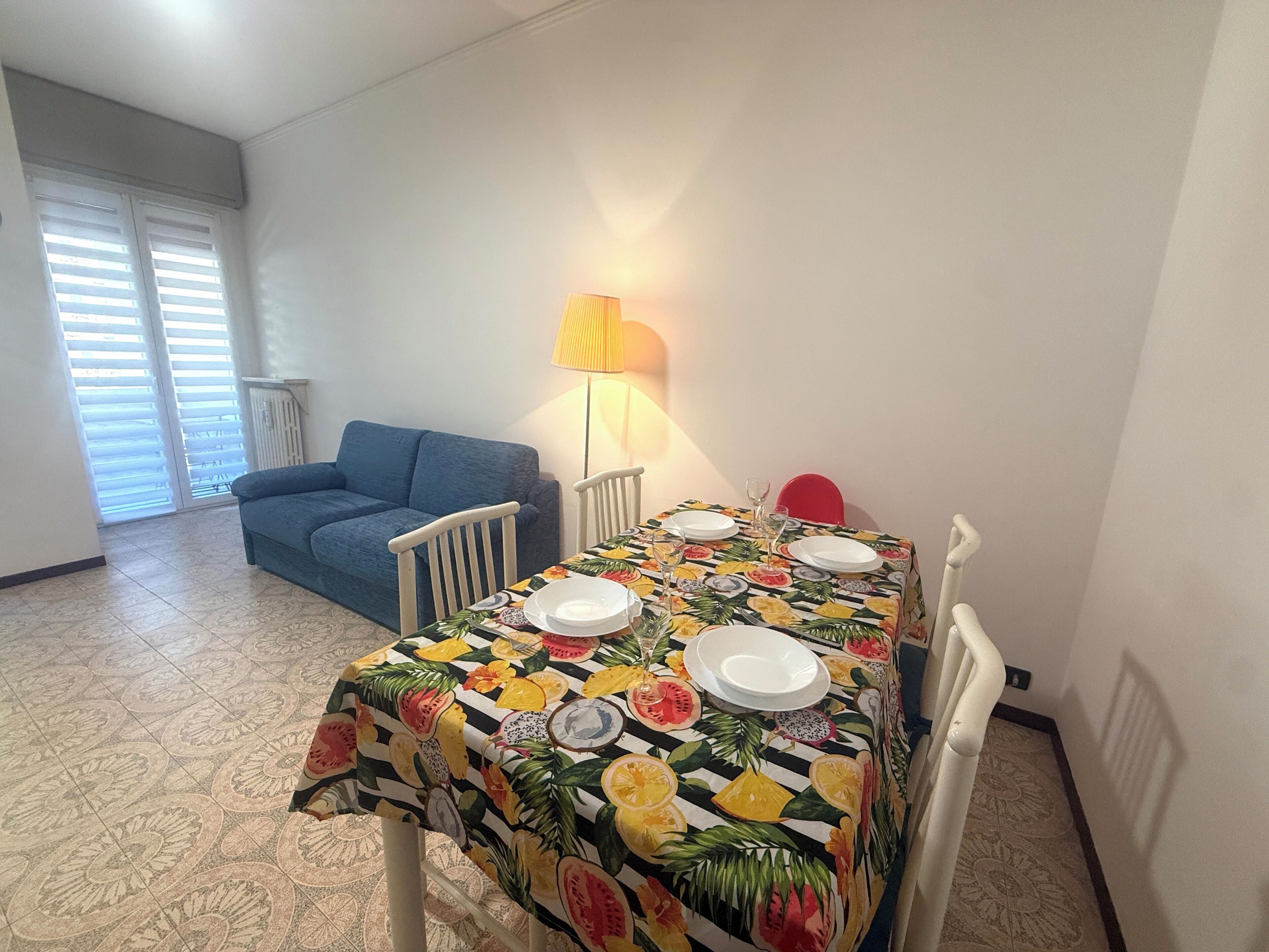 Un'area pranzo con un tavolo apparecchiato per due persone, un divano e una lampada.