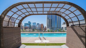 A pool area with a view of a city skyline, a covered seating area, and two small tables. - Saiya  1120 (Phoenix)