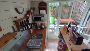 A kitchen with a microwave, kettle, and sink. There is a wooden shelf with kitchen utensils and a sign above it.