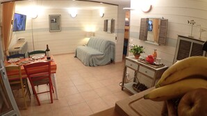 A room with a dining table set for two, a sofa, a small cabinet with a plant, and a mirror.
