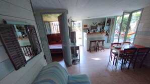 A cozy living room with a striped sofa, a dining area with a table and chairs, and a kitchen area with a counter and stools.