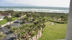 A view of a coastal area with a parking lot, palm trees, and a building with a red roof. - 
Amazing waterfront condo with an amazing view of the beach, an amazing sunrise (Palm Coast)