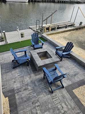Eine Terrasse mit Adirondack-Stühlen, einer Feuerstelle und Blick auf das Wasser.