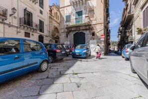 Una calle estrecha con coches aparcados y un peatón caminando.