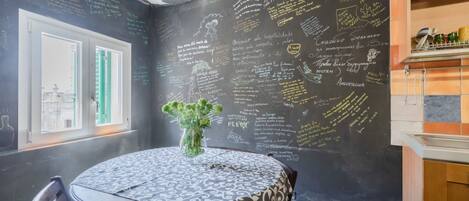 A dining area with a round table, chairs, and a blackboard wall with writings.