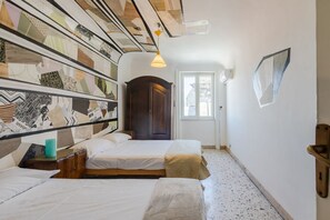 Ein Zimmer mit zwei Betten, einem Holzschrank, einer Tür und einer Wand mit ornamentalem Wandpapier.