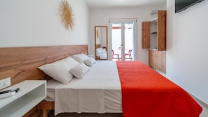 A bedroom with a wooden headboard, a bed with white bedding and a red blanket, a white bedside table, a mirror, and a TV mounted on the wall.