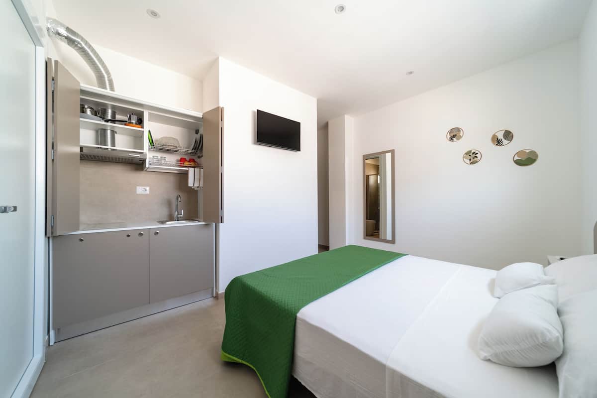 A modern hotel room with a kitchenette, a bed with white linens, and a wall-mounted TV.