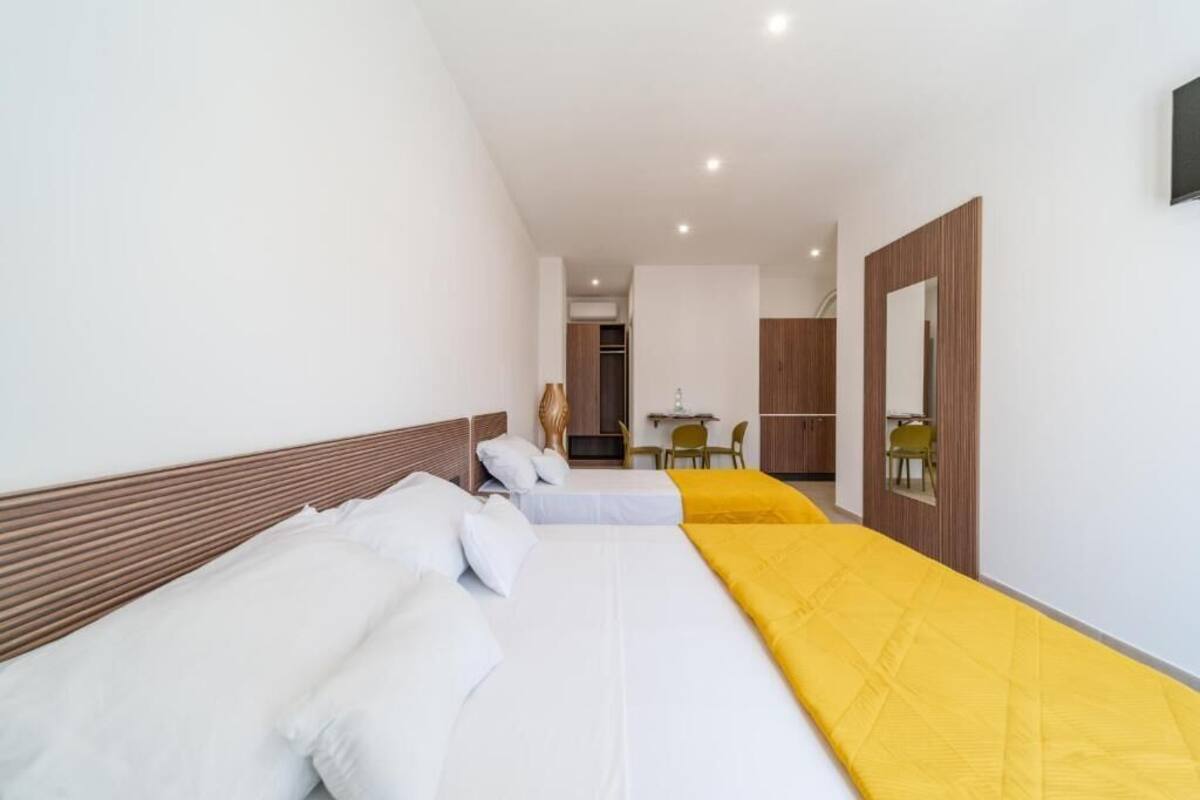 A hotel room with two beds, a wooden headboard, a yellow bed runner, and a small desk with a chair.