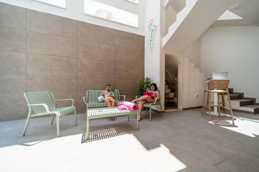 Un espace intérieur spacieux comprenant deux fauteuils verts et un banc, un escalier et un bureau avec une chaise.