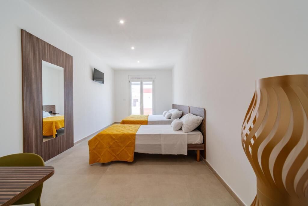 A hotel room with two beds, a mirror, a television, and a large decorative vase.
