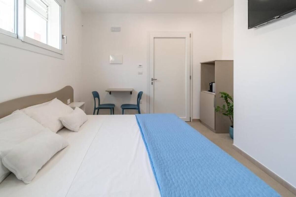 A bedroom with a bed, a desk, two chairs, a TV, and a door.