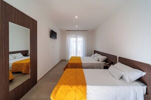 A hotel room with two beds, a large mirror, and a view of the outside through a window with curtains.