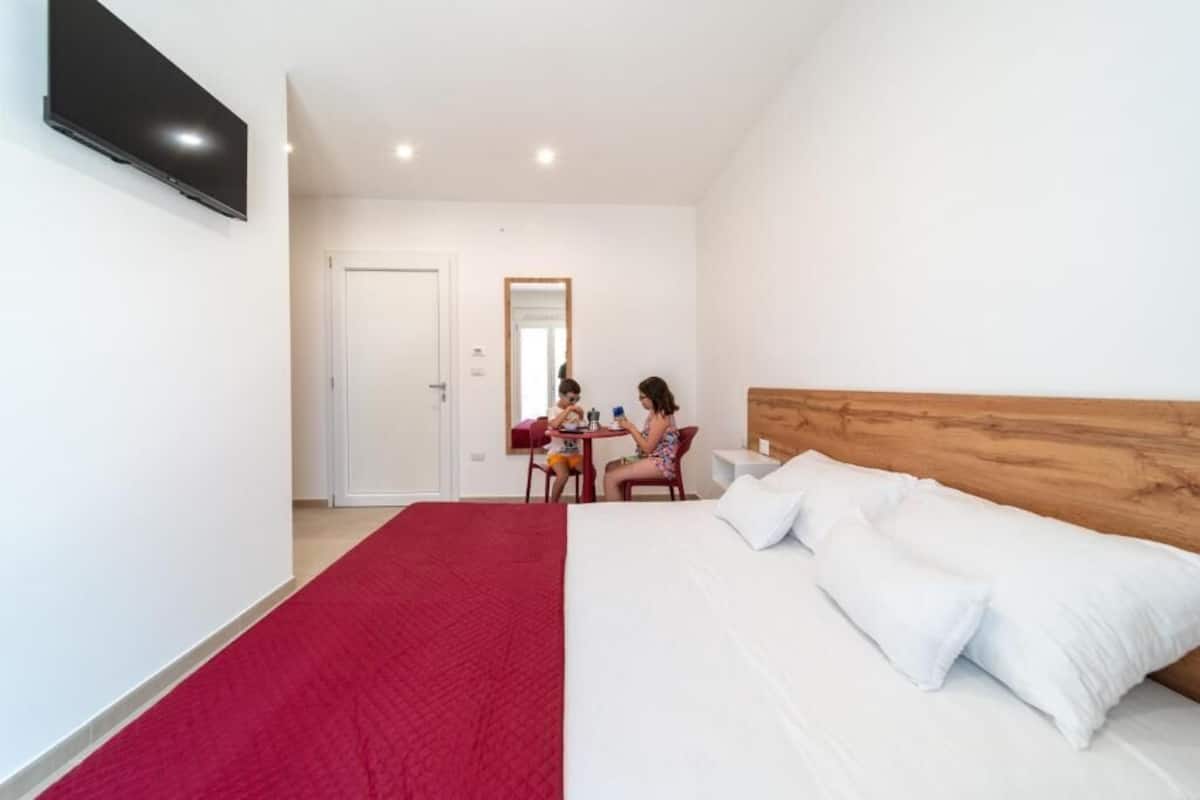 A hotel room with a large bed, a TV mounted on the wall, and a red carpet.