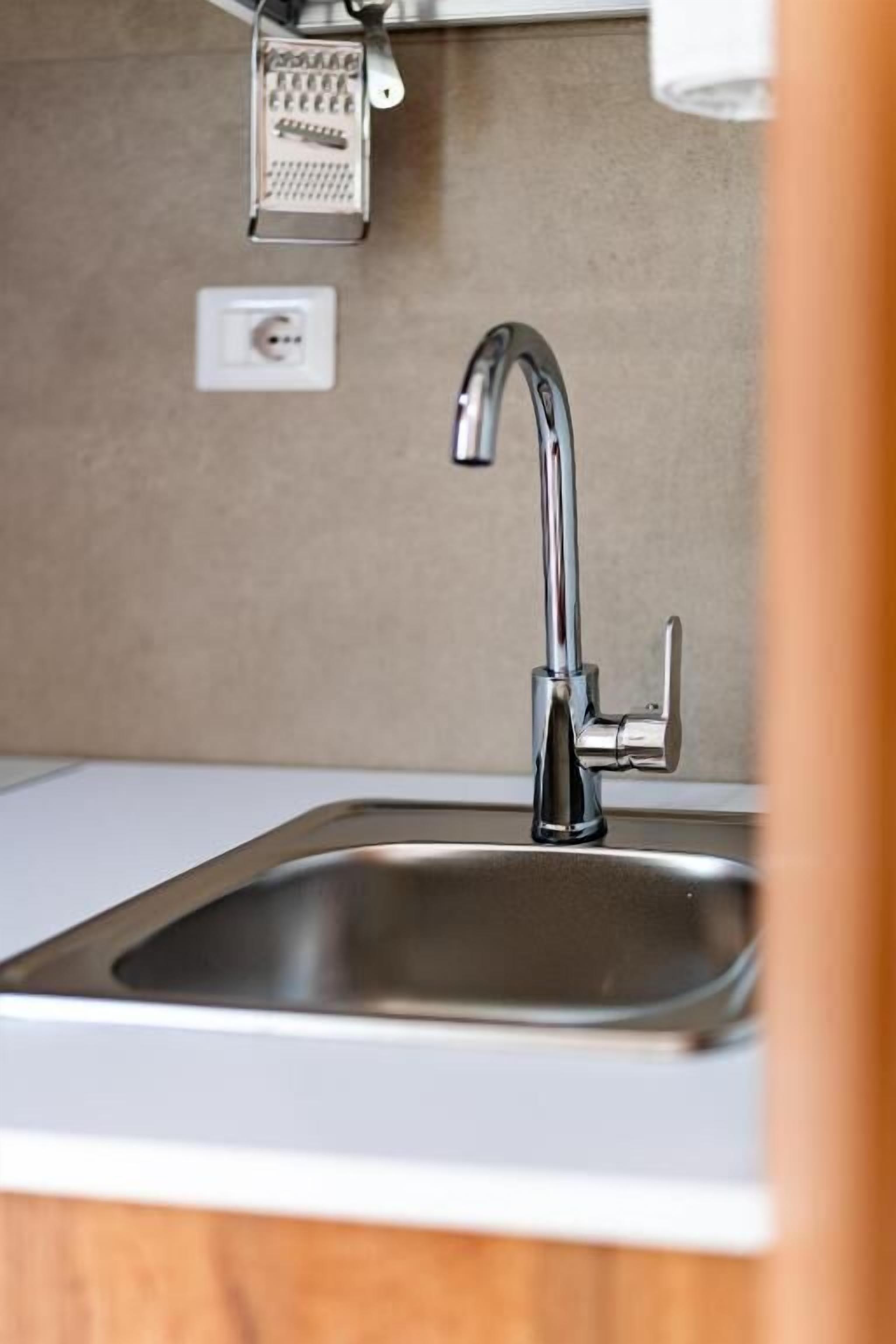 A kitchen sink with a modern faucet, a built-in grater, and a wall-mounted light switch.