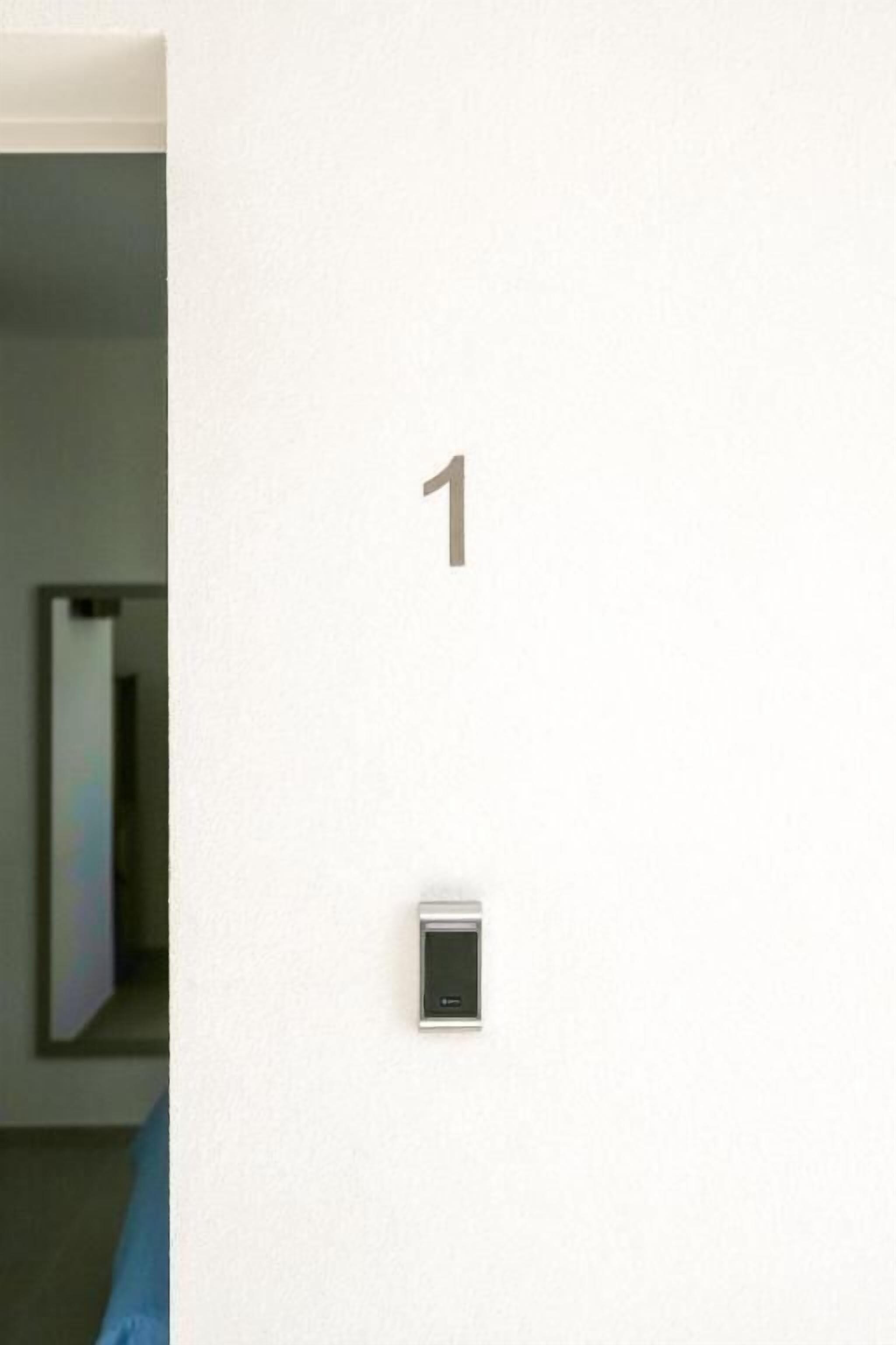 Une pièce avec un mur blanc, une porte et un petit appareil numérique fixé au mur.