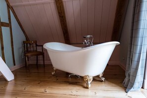 Une baignoire à pieds de couleur blanche, dans une pièce au plancher en bois et au plafond en pente.