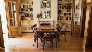 A room with a wooden floor, a central table with chairs, bookshelves, and a fireplace. - Alcor Exclusive Friedrichsruh (Aumuehle)